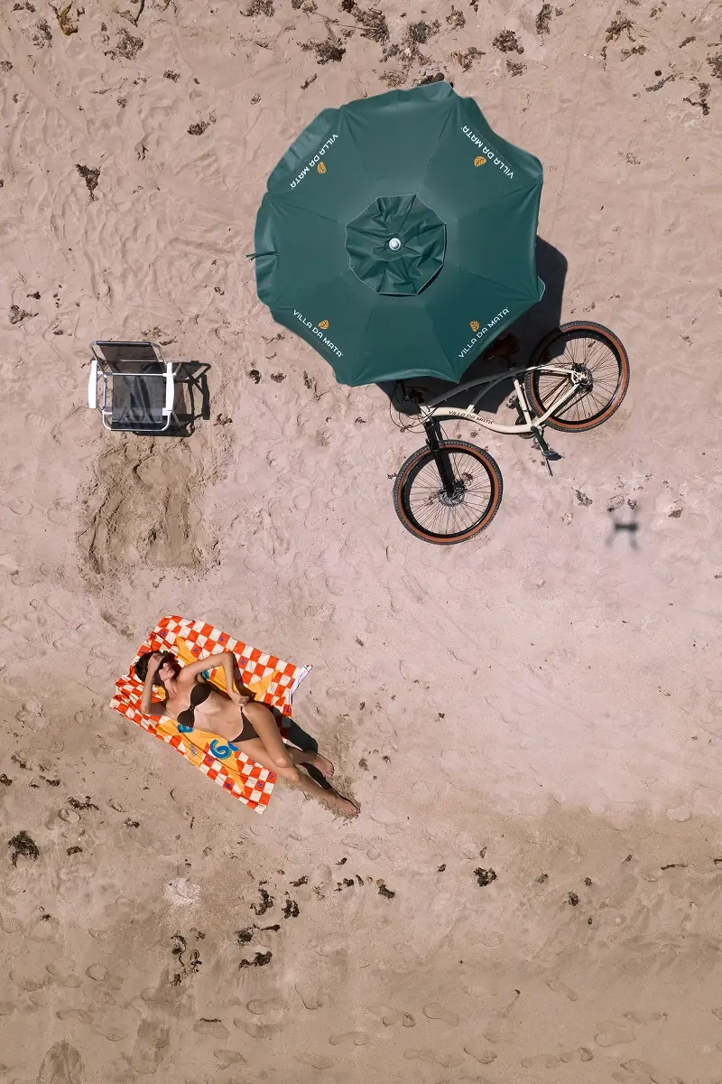 Bicicleta, guarda-sol e canga na areia da Praia do Riacho, vistos de cima